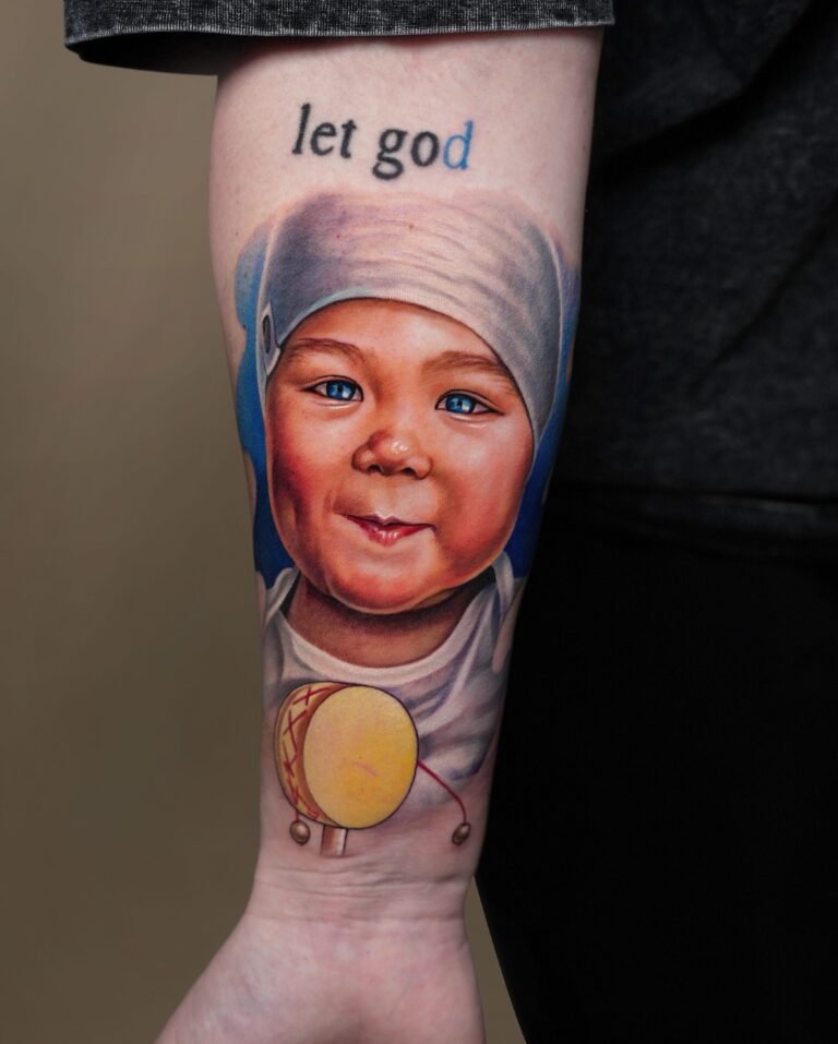 Realistic color portrait tattoo of a smiling baby holding a toy drum on a forearm sleeve